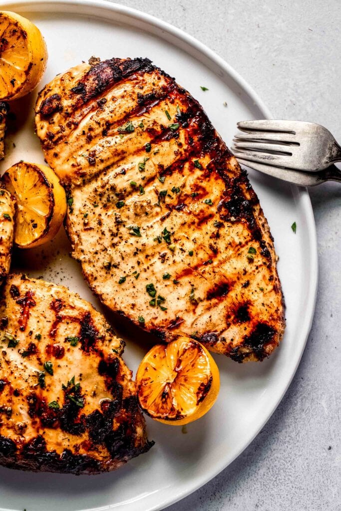 Grilled whole chicken breasts on plate with lemons. 