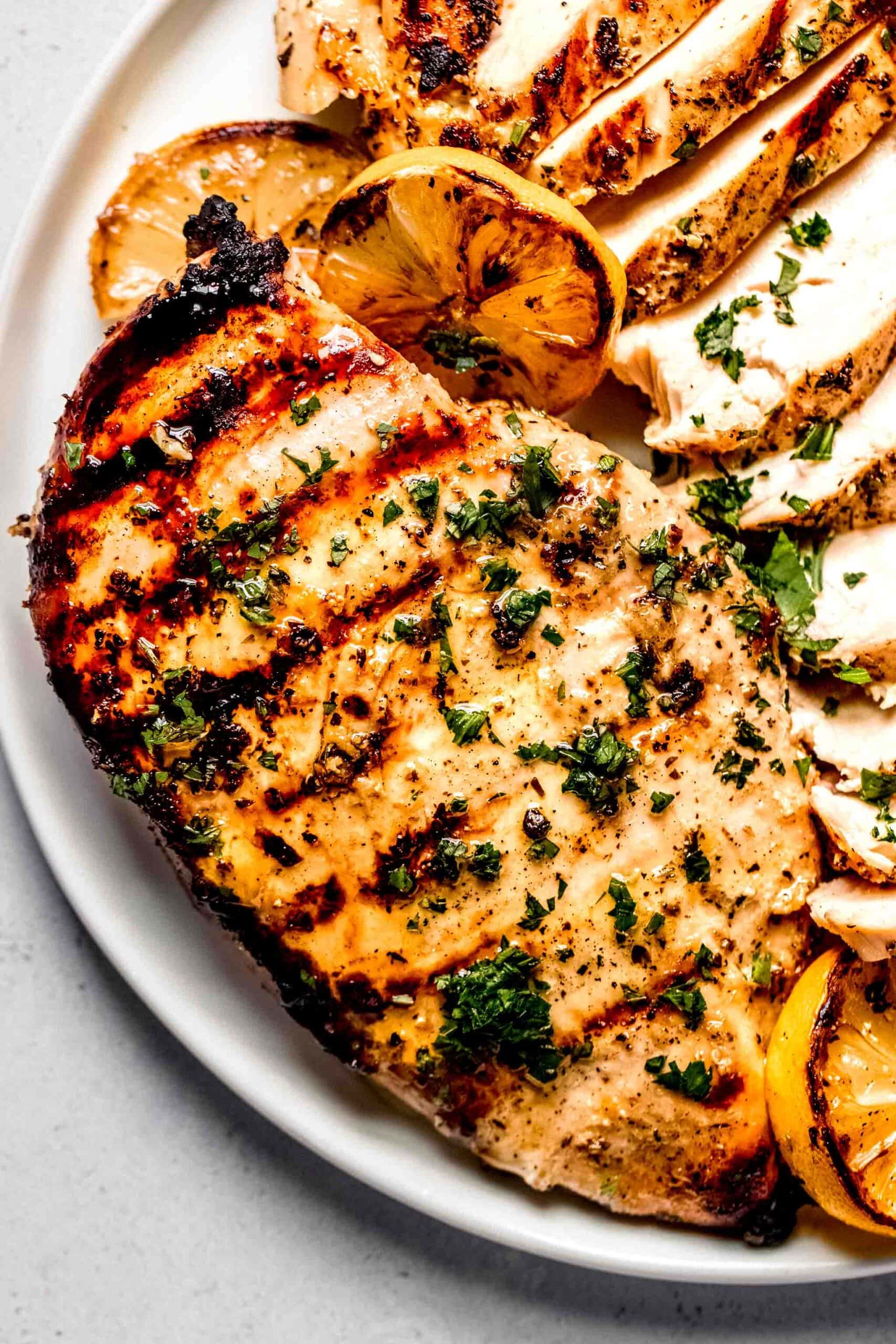 Greek marinated chicken breasts on plate, one sliced.