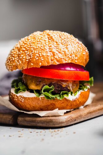 Side view of smoked burger topped with tomato, lettuce & cheese.