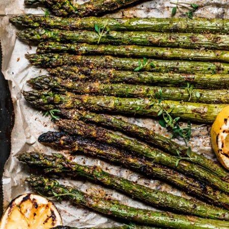 Smoked asparagus spears on baking sheet with parchment and charred lemons.