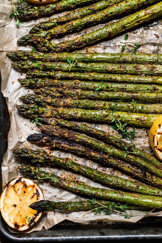Smoked asparagus spears on baking sheet with parchment and charred lemons.