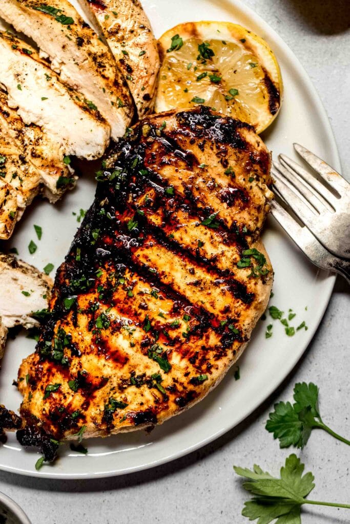 Close up of chicken breast with grill marks next to piece of sliced chicken.