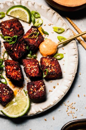 Finished air fryer salmon bites on plate with sesame seeds and green onions, and a spoonful of chipotle crema.