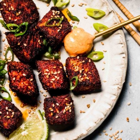 Finished air fryer salmon bites on plate with sesame seeds and green onions, and a spoonful of chipotle crema.