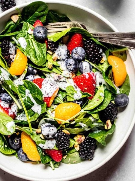 Prepared berry spinach salad in white bowl with dressing drizzled on top.