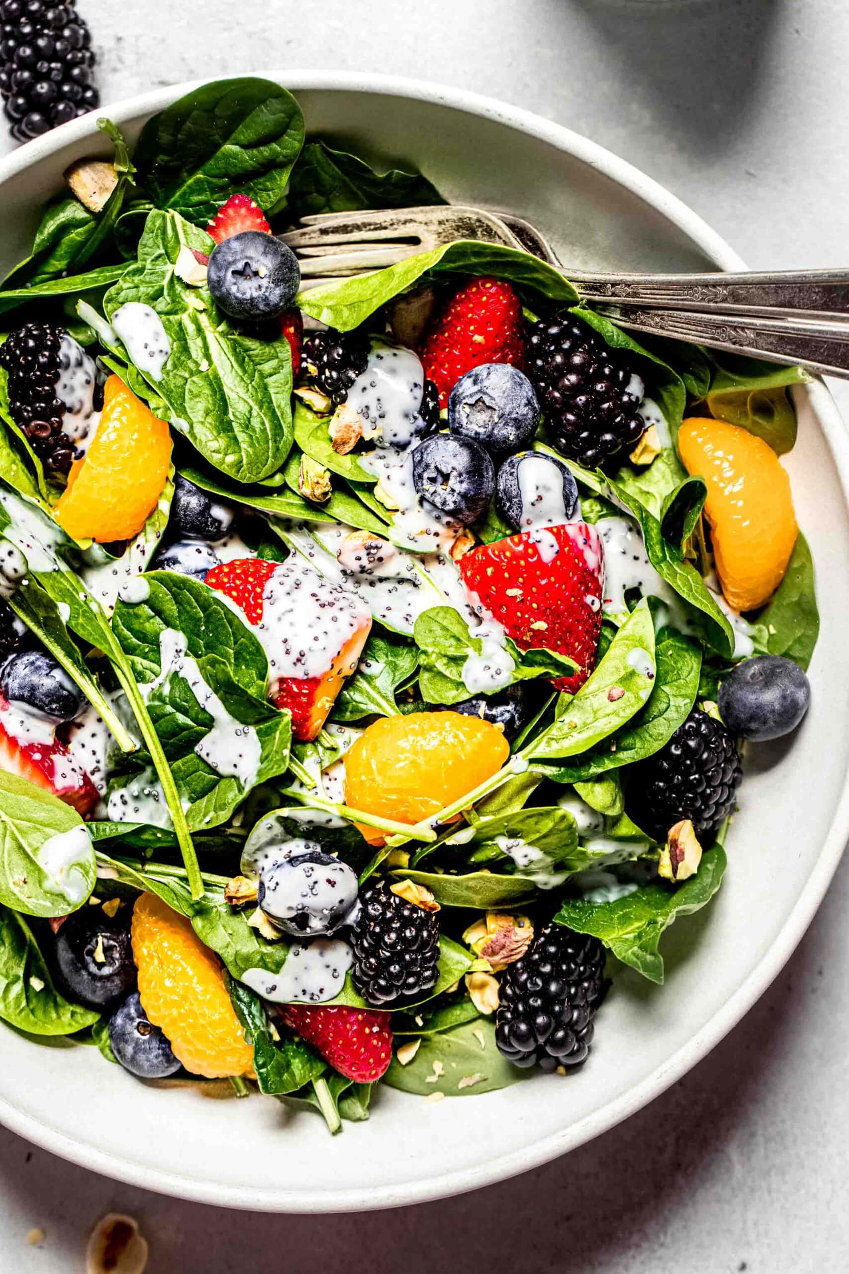 Prepared berry spinach salad in white bowl with dressing drizzled on top.