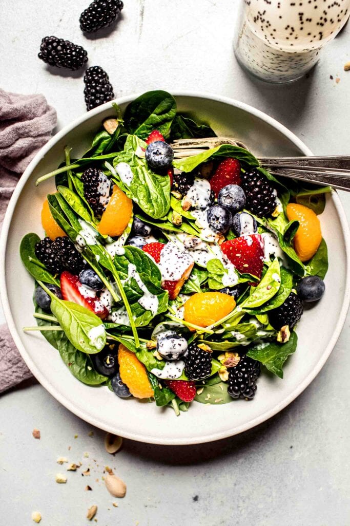 Overhead shot of prepared salad in white bowl with berries scattered around.