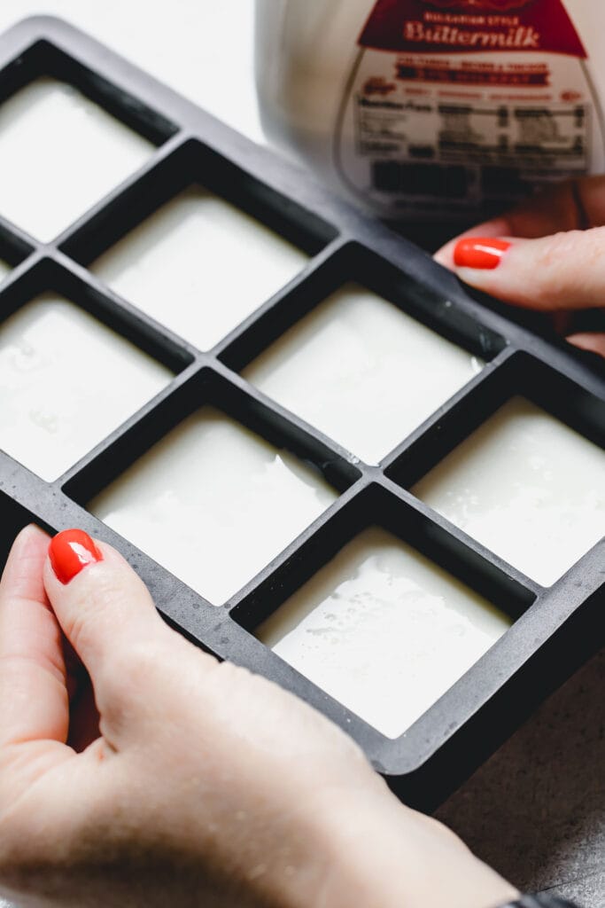 Hands holding ice cube tray filled with buttermilk. 