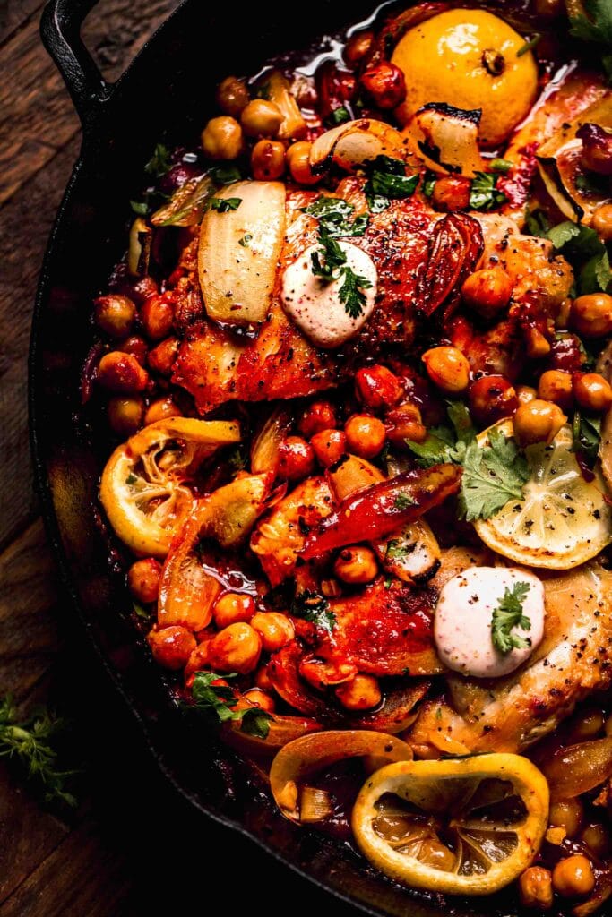 Harissa chicken and chickpeas cooked in skillet topped with yogurt sauce. 