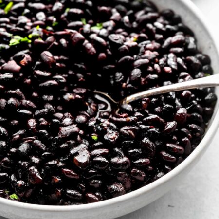 Side view of seasoned black beans in bowl with spoon.