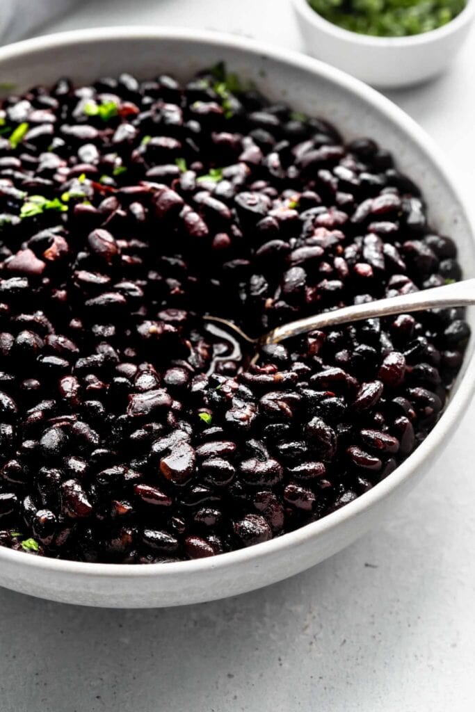 Side view of seasoned black beans in bowl with spoon. 