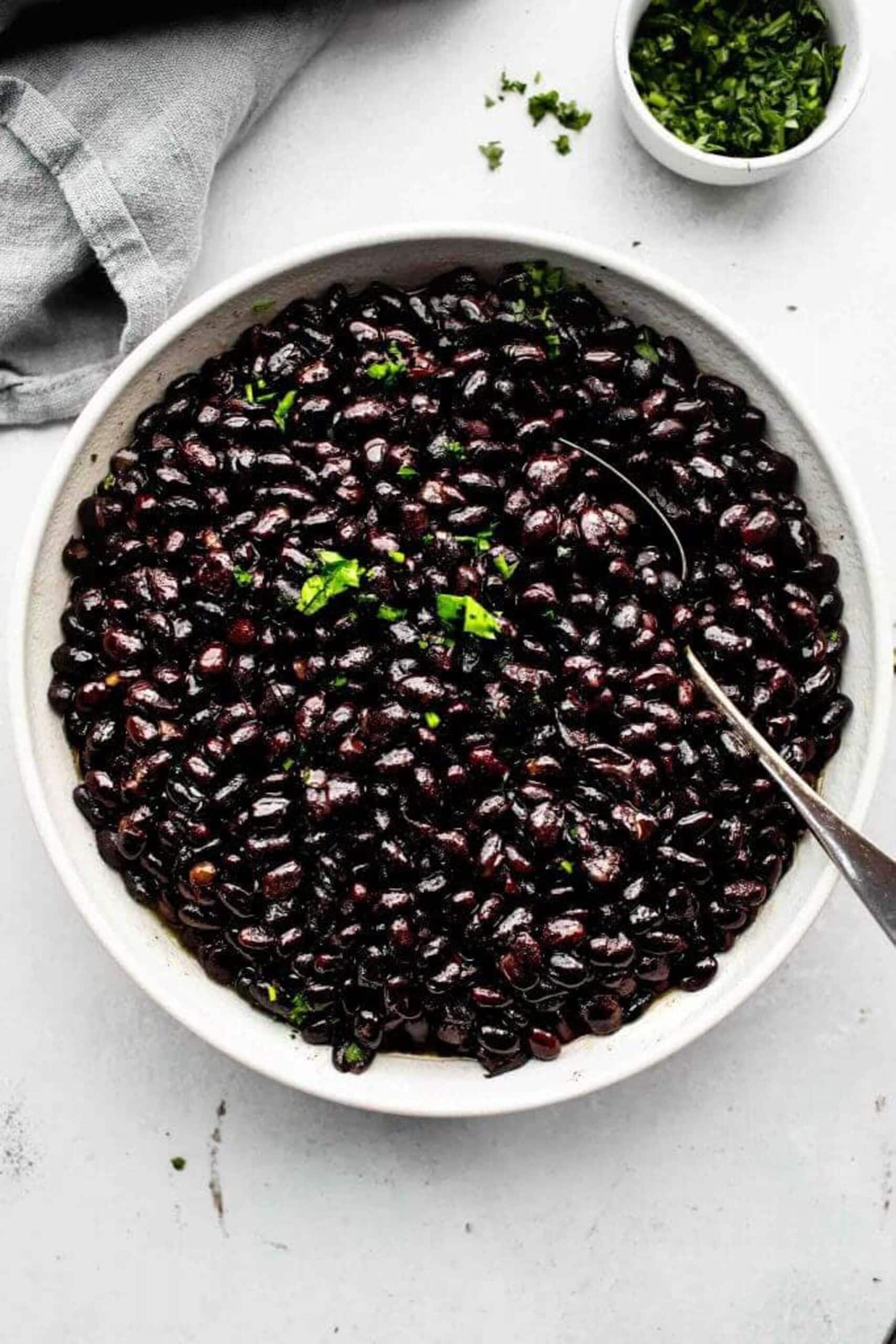 Overhead shot of seasoned black beans in white bowl with spoon.