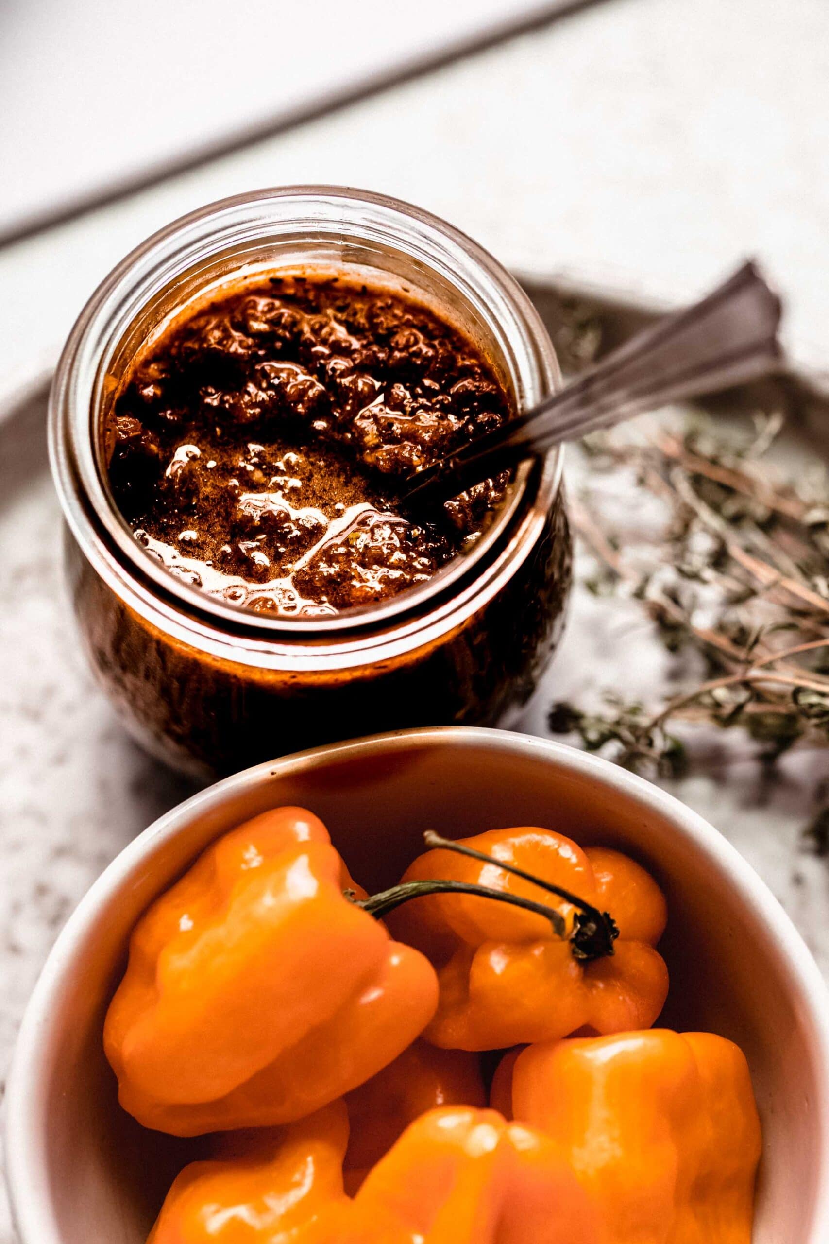 Side view of jar of jerk sauce next to bowl of habaneros.