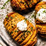 Hasselback potatoes on grey plate dolloped with sour cream.