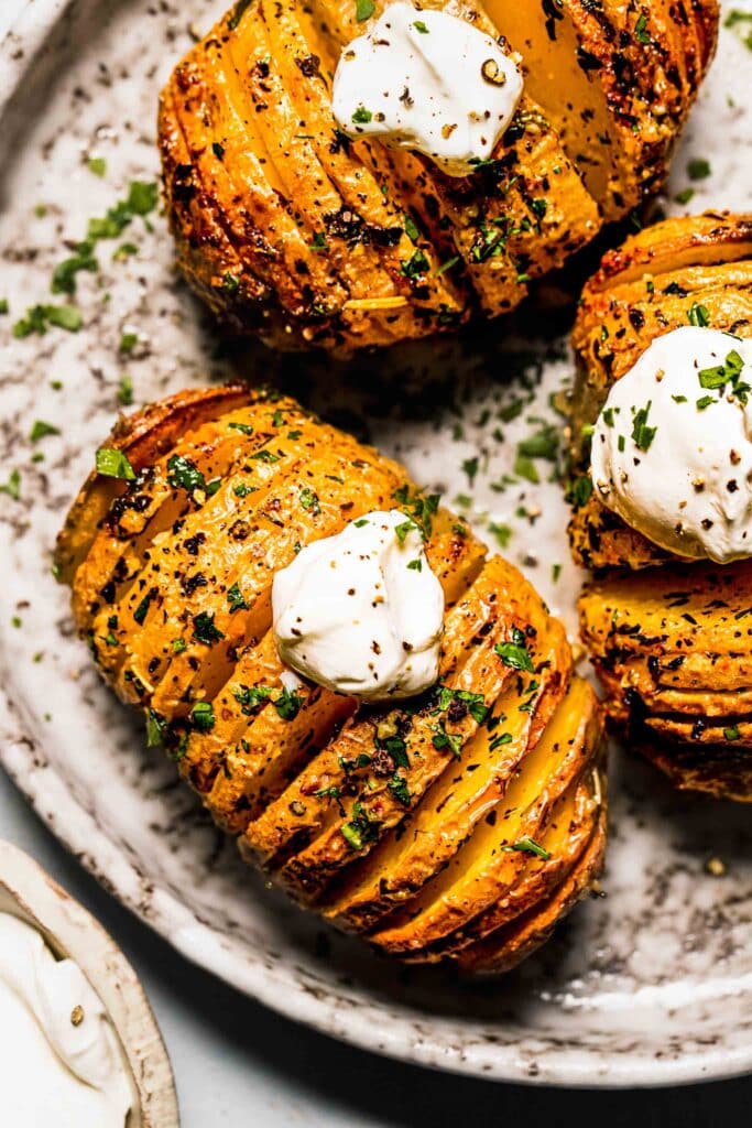Hasselback potatoes on grey plate dolloped with sour cream.