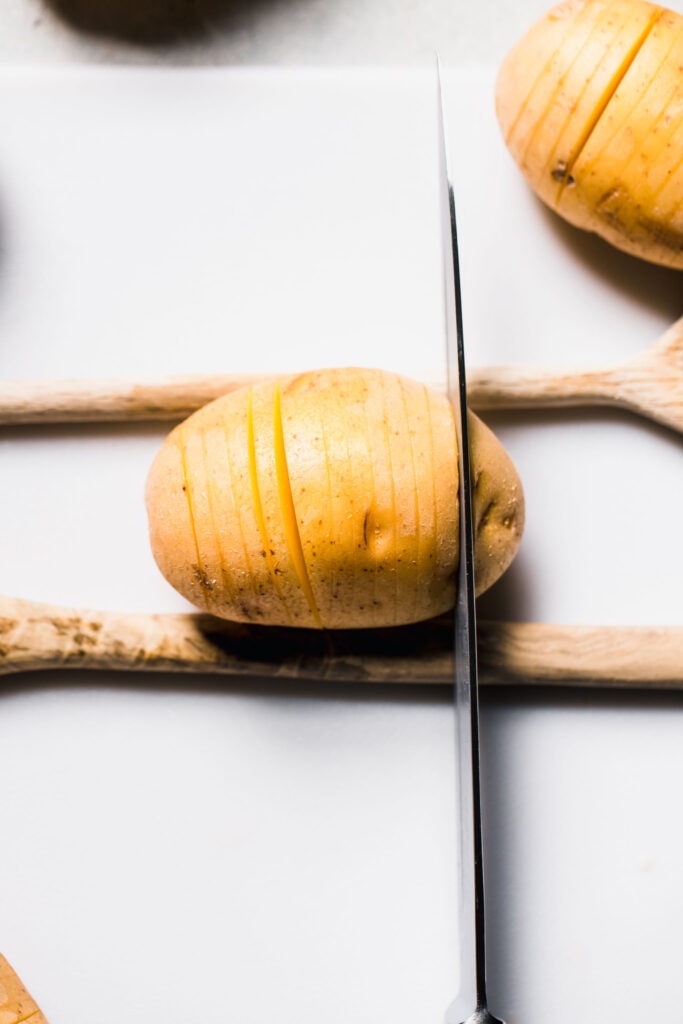 Potato wedged between two wooden spoons being sliced.