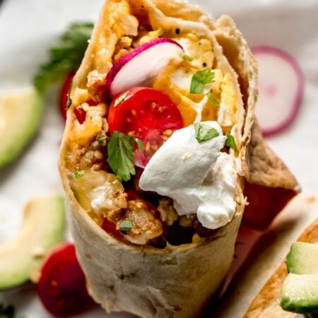 Halved breakfast burrito topped with sour cream.