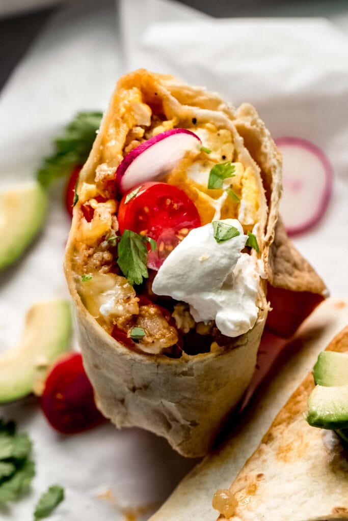 Halved breakfast burrito topped with sour cream.