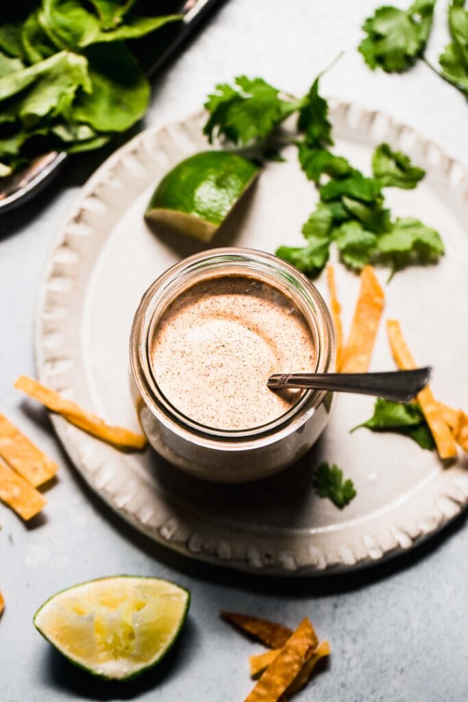 Jar of southwest salad dressing next to cilantro leaves and lime wedges. 