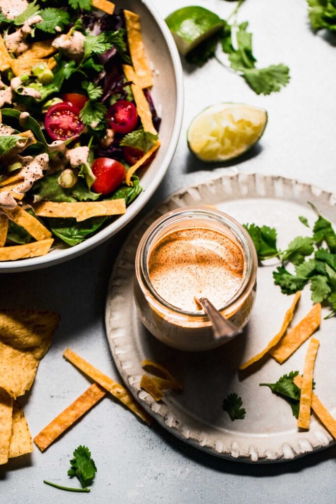 Jar of southwest salad dressing next to green salad with tortilla strips. 