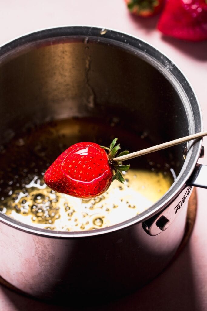 Strawberry on skewer being dipped into sugar mixture.