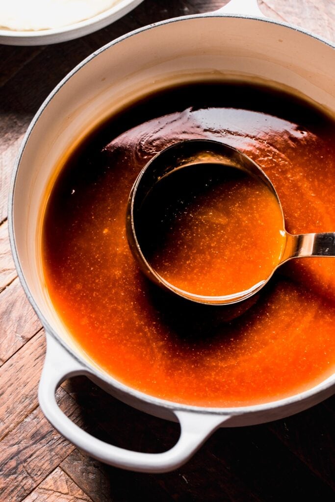 Beef gravy in saucepan with ladle.