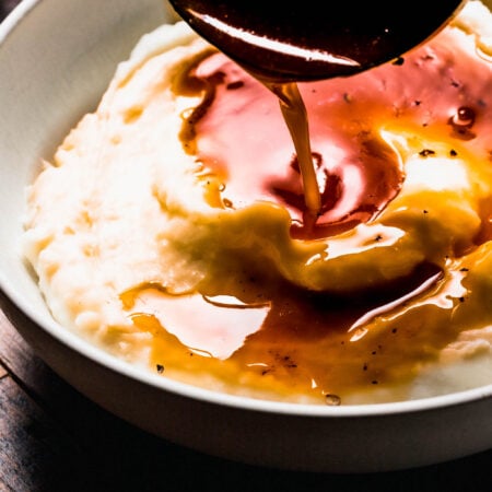 Ladle pouring beef gravy onto bowl of mashed potatoes.