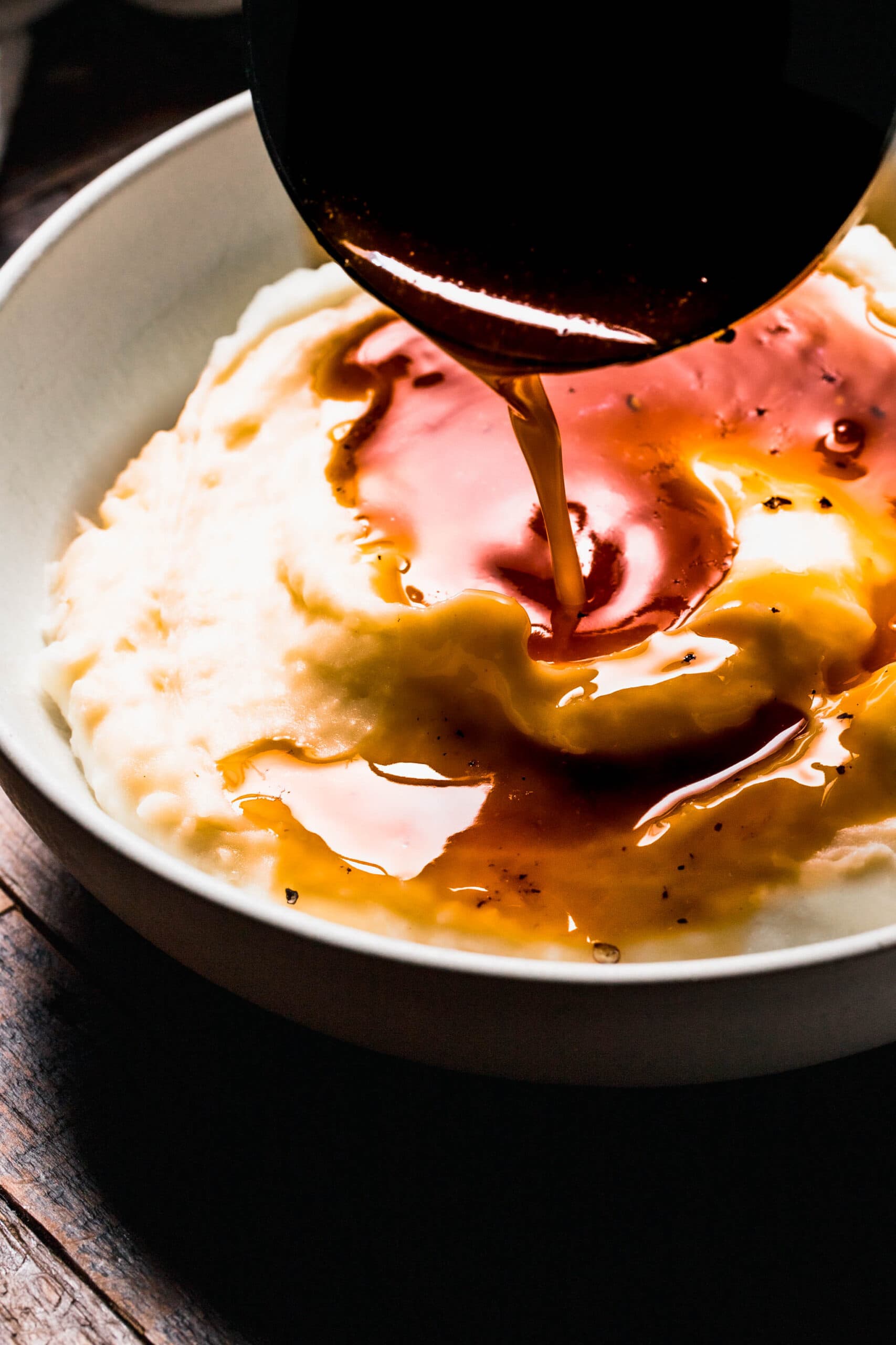 Ladle pouring beef gravy onto bowl of mashed potatoes.