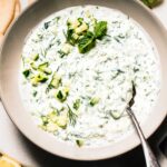 Overhead shot of prepared tzatziki sauce in bowl surrounded by pita bread.