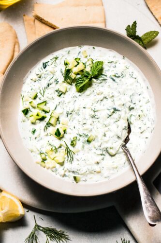 Overhead shot of prepared tzatziki sauce in bowl surrounded by pita bread.