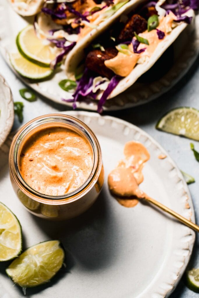 Fish taco sauce in small jar with spoon next to baja fish tacos.