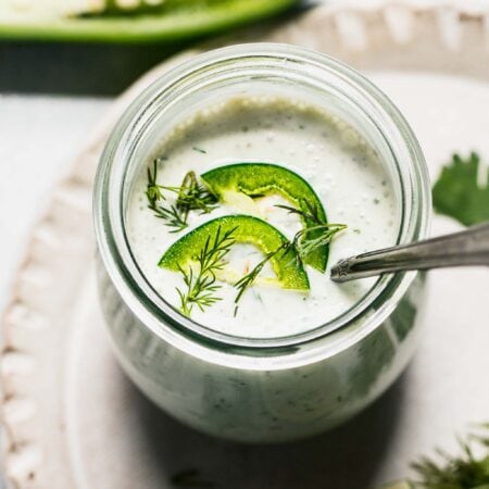 Overhead shot of jalapeno ranch in small jar with spoon, topped with sliced jalapenos.