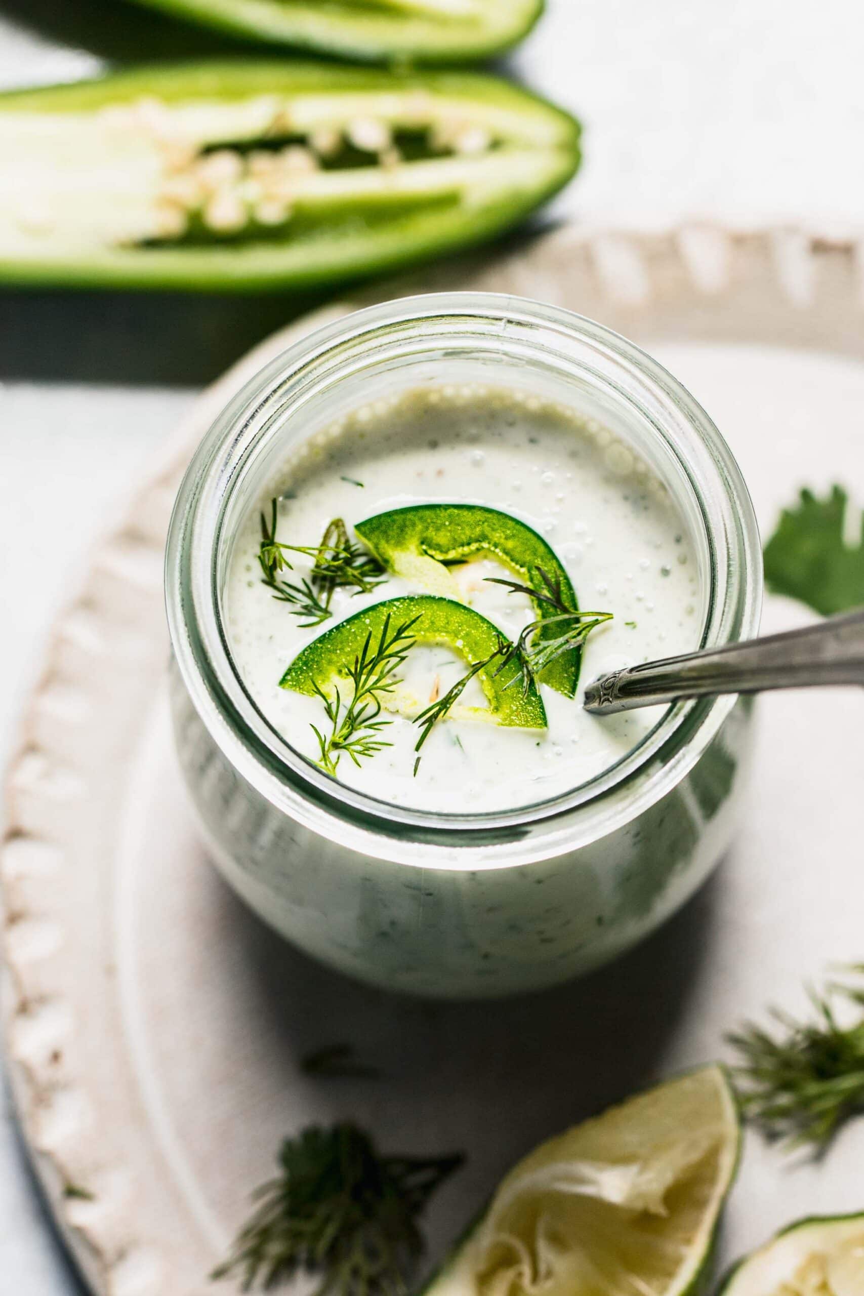 Overhead shot of jalapeno ranch in small jar with spoon, topped with sliced jalapenos.