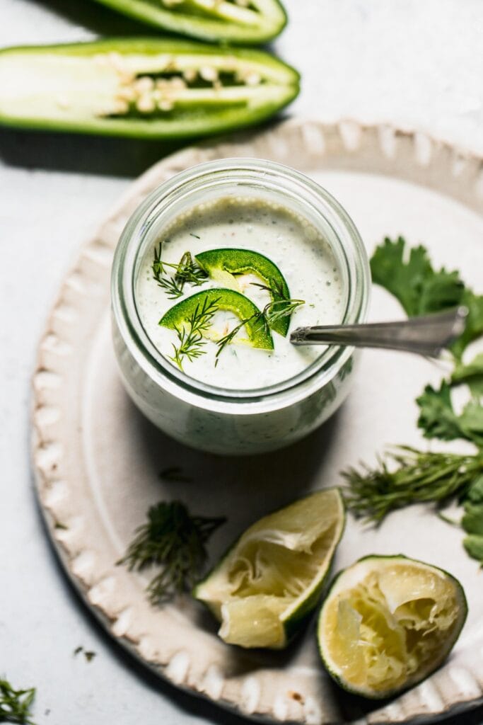 Jalapeno ranch in small jar with spoon, topped with sliced jalapenos.