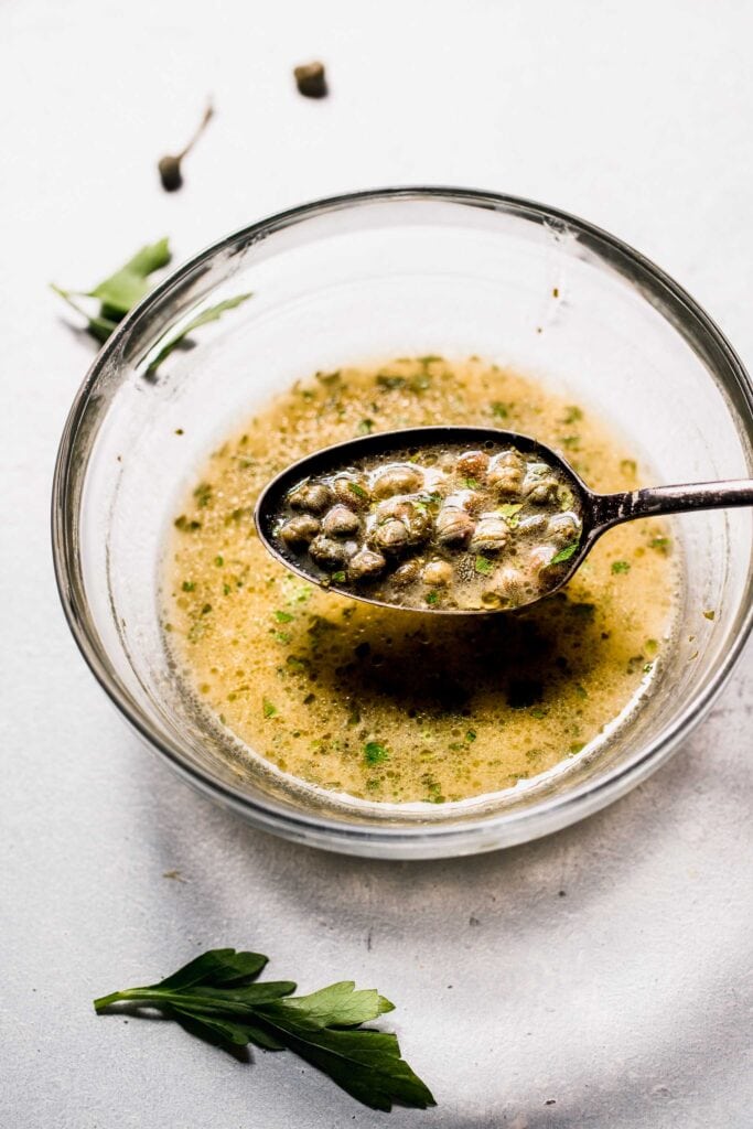 Lemon caper sauce in bowl with spoon. 