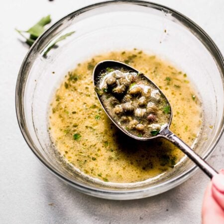 Lemon caper sauce on spoon over small bowl.