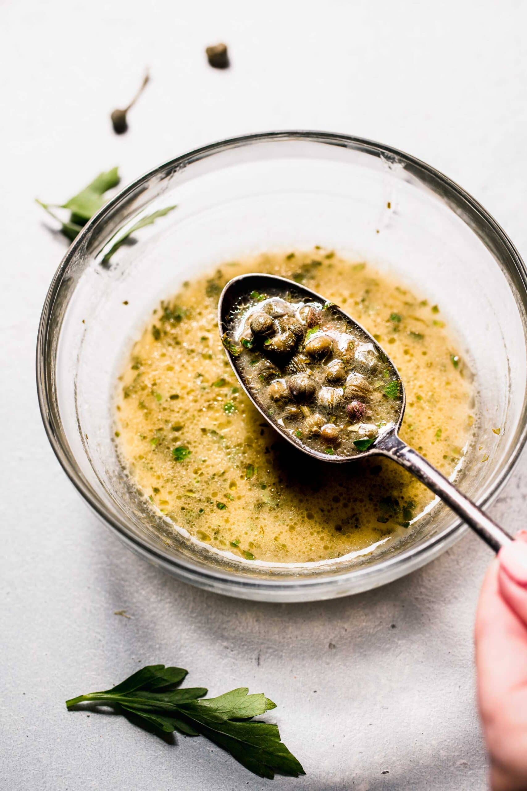 Lemon caper sauce on spoon over small bowl.