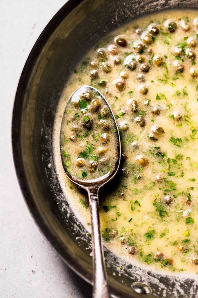 Lemon caper sauce in skillet with spoon. 