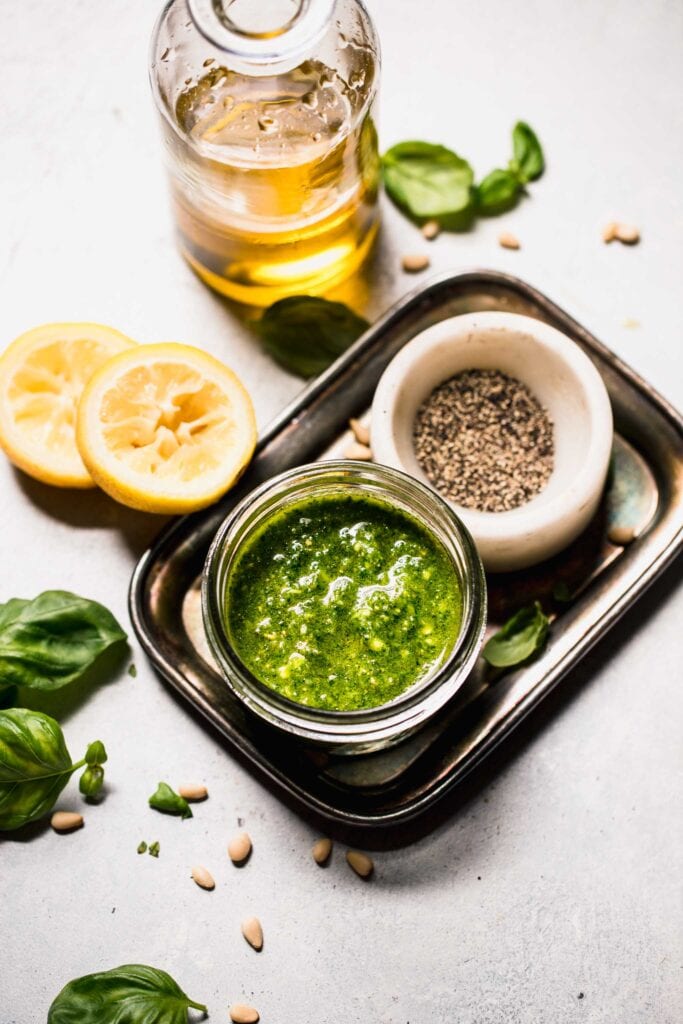 Pesto in small bowl next to olive oil and lemons. 