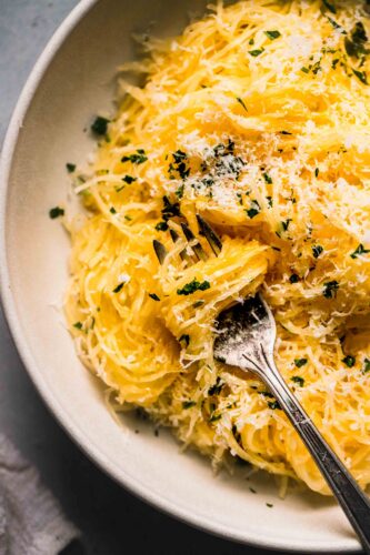 Prepared spaghetti squash in bowl topped with parsley & parmesan.