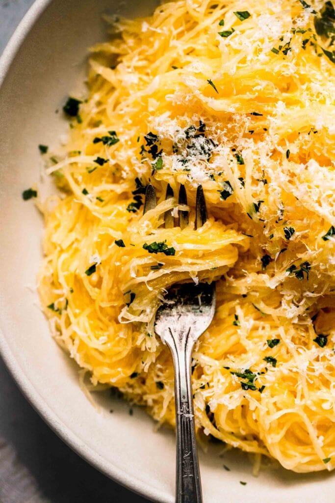 Prepared spaghetti squash in bowl with fork topped with parsley & parmesan.