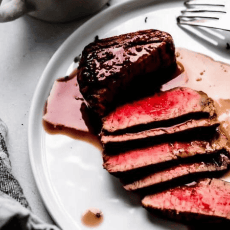 Sliced steak on plate with red wine sauce.
