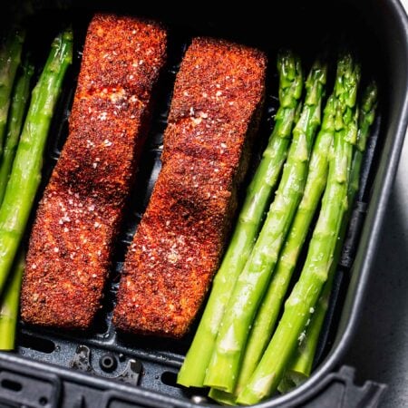Salmon filets and asparagus in air fryer basket.