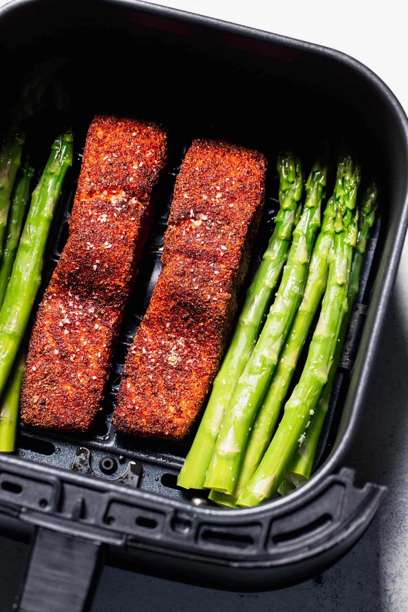 Salmon filets and asparagus in air fryer basket.