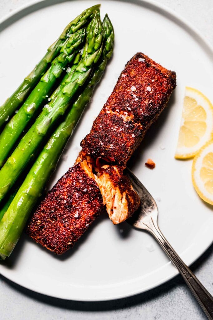 Air fryer salmon on plate with asparagus and lemon wedges. 