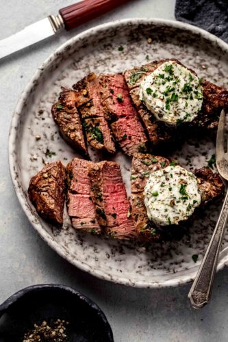 Two sliced air fryer filet mignons topped with garlic butter on plate.