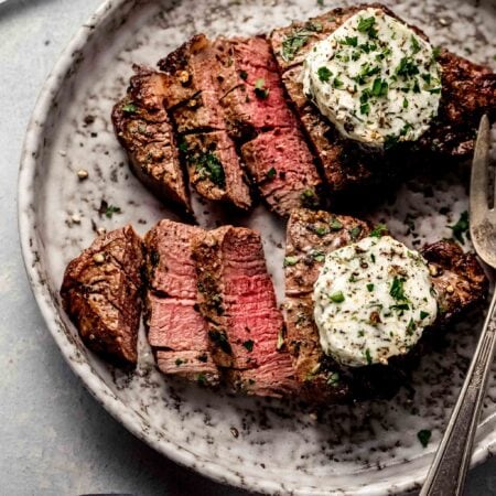 Two sliced air fryer filet mignons topped with garlic butter on plate.