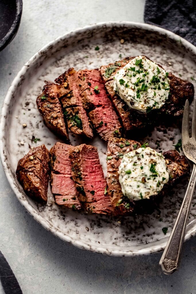 Two sliced air fryer filet mignons topped with garlic butter on plate.