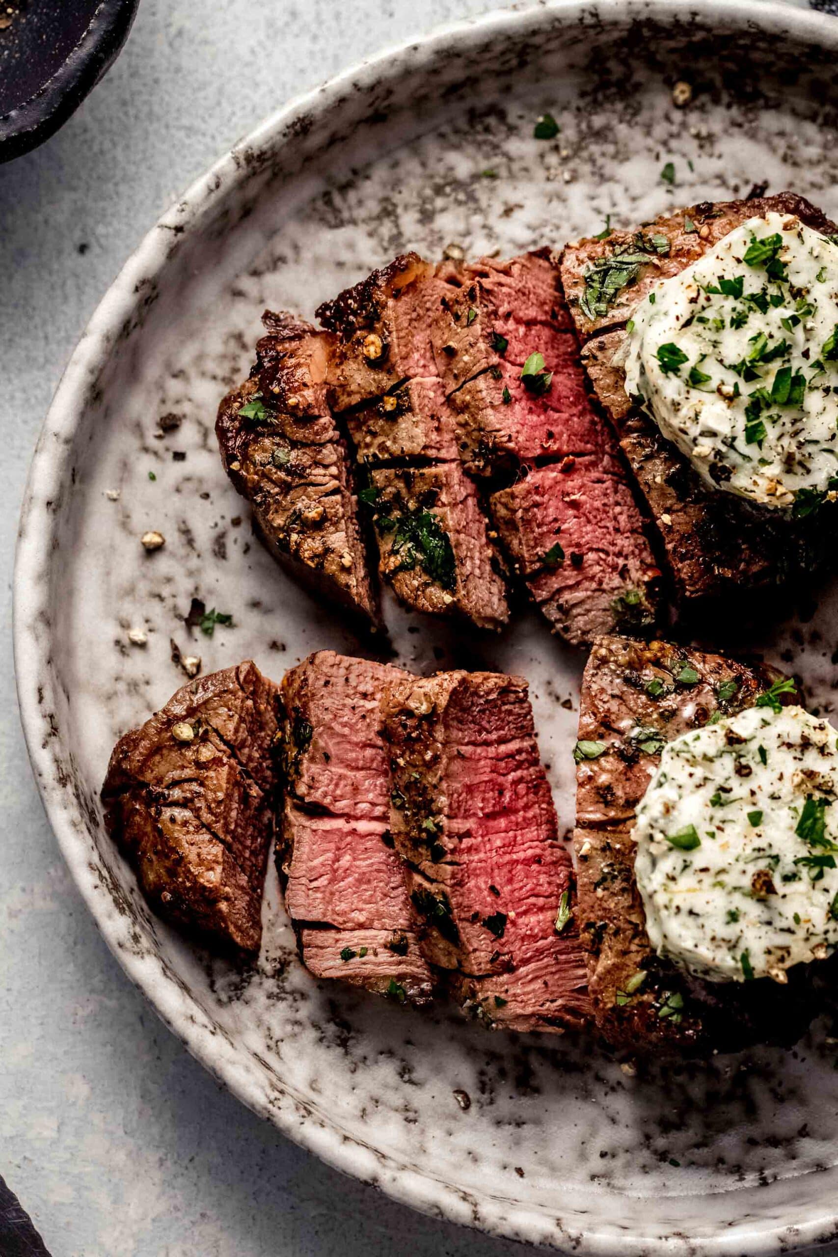 Two sliced air fryer filet mignons topped with garlic butter on plate.