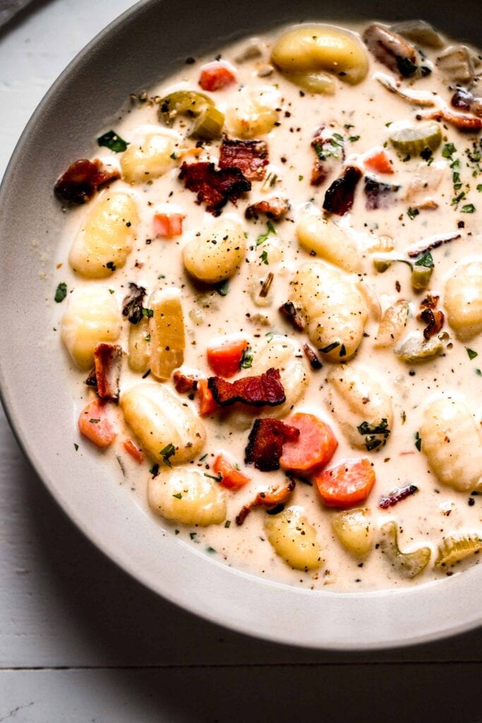 Close up of bowl of creamy gnocchi soup with crispy bacon on top. 